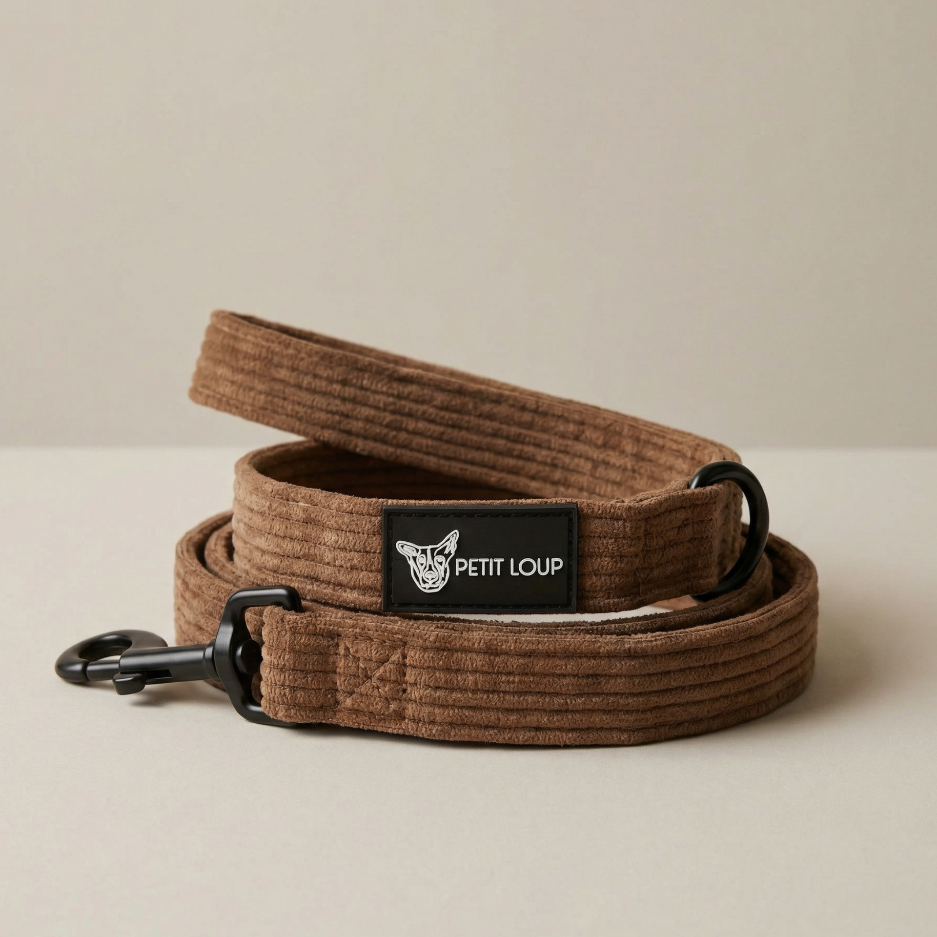 Brown dog leash with black clip and 'Petit Loup' brand label on a beige background