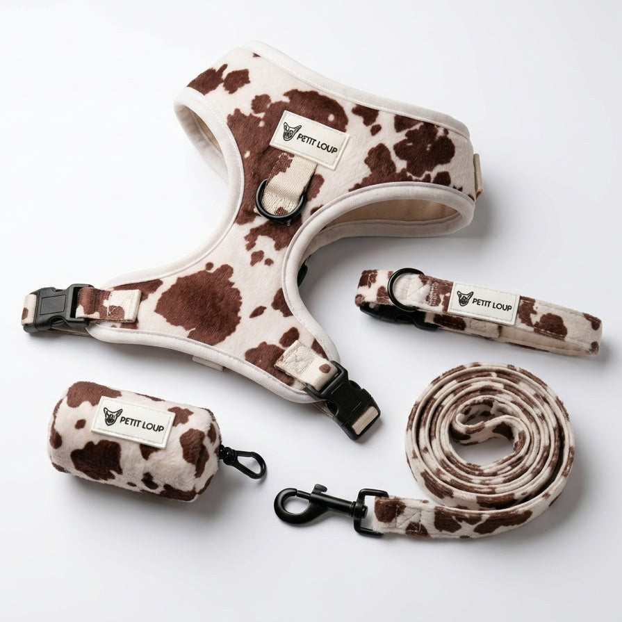 Cow print dog harness, leash, and pouch on a white background